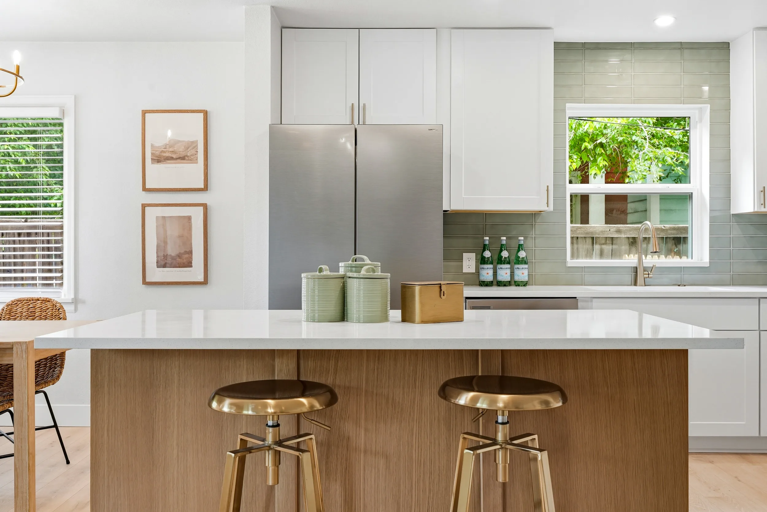 Oak island with a quartz top, brass stools and sage tile behind